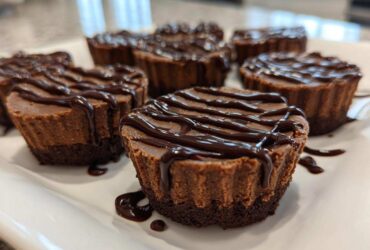 Close-up of several Keto Chocolate Peanut Butter Fat Bombs drizzled with chocolate sauce on a white platter.