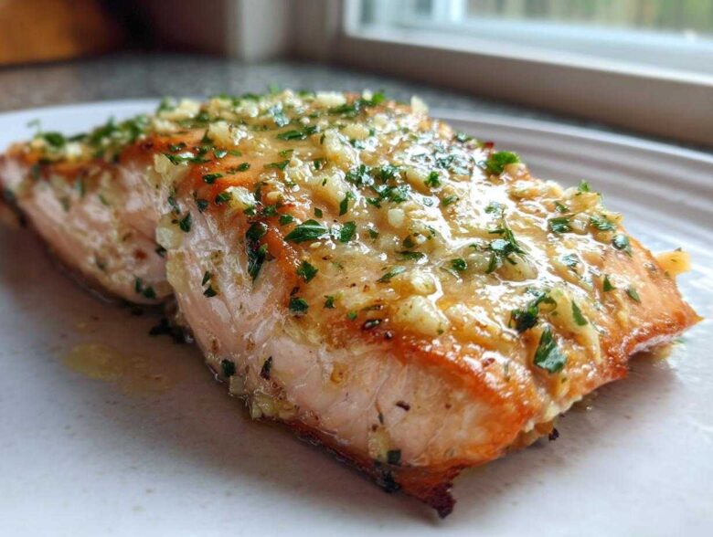 A close-up of a perfectly cooked Keto Garlic Butter Salmon fillet, glistening with butter, minced garlic, and parsley.