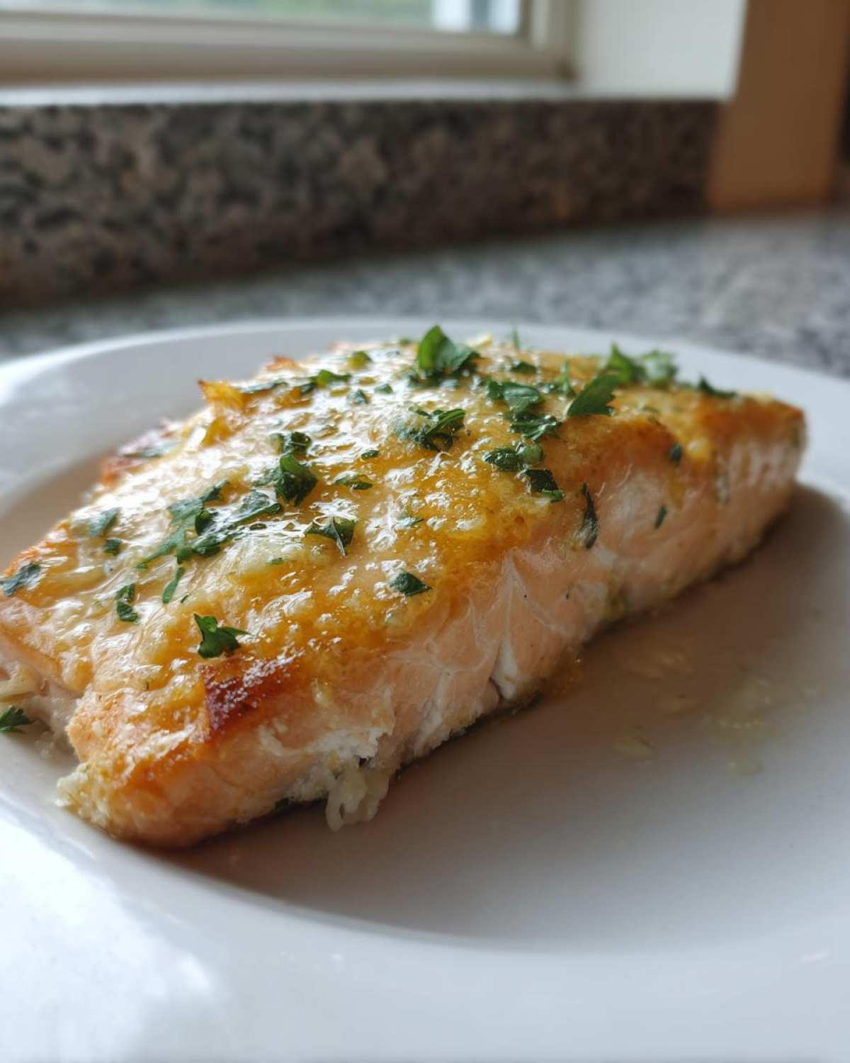 Close-up of a cooked fillet of Keto Garlic Butter Salmon topped with melted butter sauce and fresh parsley.