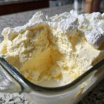 Close-up of creamy, pale yellow Keto Lemon Cheesecake Mousse topped with dollops of white whipped topping in a glass dish.