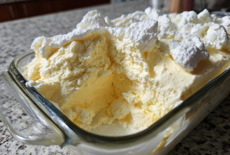 Close-up of creamy, pale yellow Keto Lemon Cheesecake Mousse topped with dollops of white whipped topping in a glass dish.