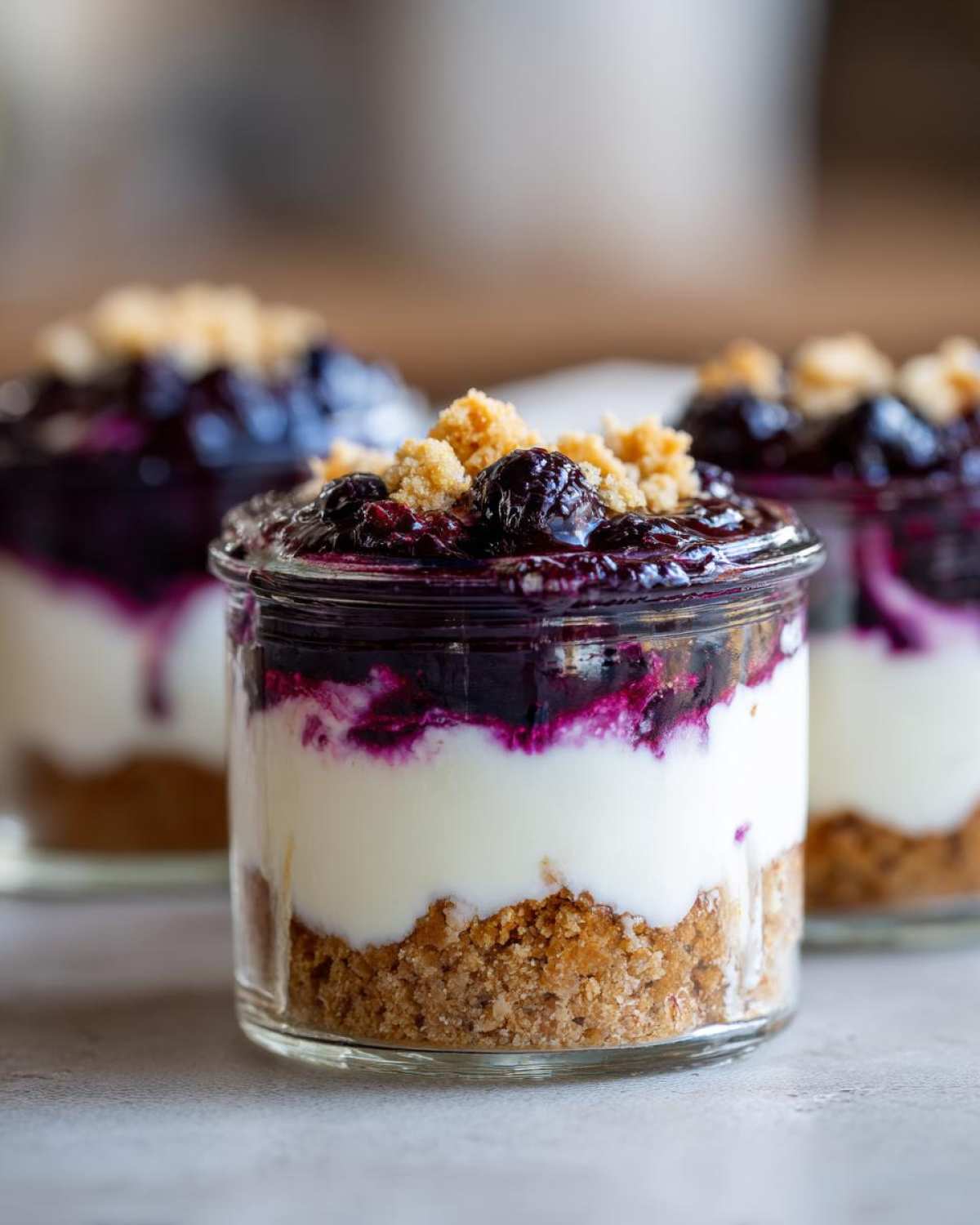 A close-up of a layered Lemon Blueberry Cheesecake Jar showing graham cracker crust, white cream cheese filling, and blueberry topping.