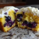Close-up of a Lemon Blueberry Cupcakes with Cream Cheese Frosting cut in half showing moist cake and berries.