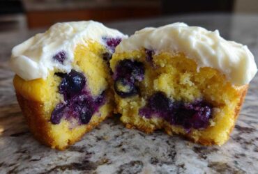 Close-up of a Lemon Blueberry Cupcakes with Cream Cheese Frosting cut in half showing moist cake and berries.