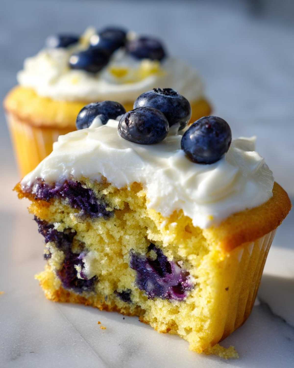 Close-up of a Lemon Blueberry Cupcake with Cream Cheese Frosting, showing the moist yellow cake and burst blueberries inside.