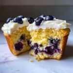 Close-up of a Lemon Blueberry Cupcakes with Cream Cheese Frosting cut in half, showing moist cake and juicy blueberries.