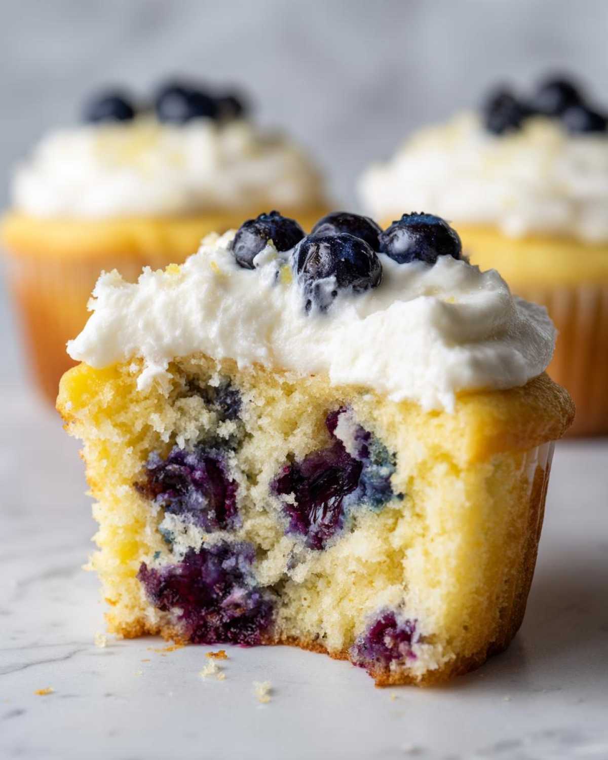 Close-up of a Lemon Blueberry Cupcakes with Cream Cheese Frosting cut in half, showing moist cake and burst blueberries.
