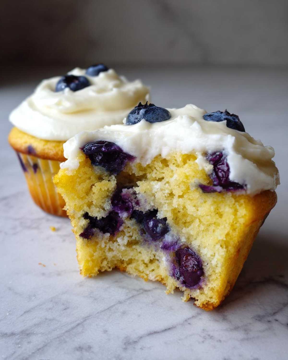 Close-up of a Lemon Blueberry Cupcakes with Cream Cheese Frosting, cut in half to show moist interior and blueberries.