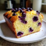 Close-up of a moist slice of Lemon Blueberry Yogurt Loaf showing bright yellow crumb and bursting blueberries.