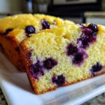 Close-up of a slice of moist Lemon Blueberry Yogurt Loaf showing bright yellow crumb and burst blueberries.
