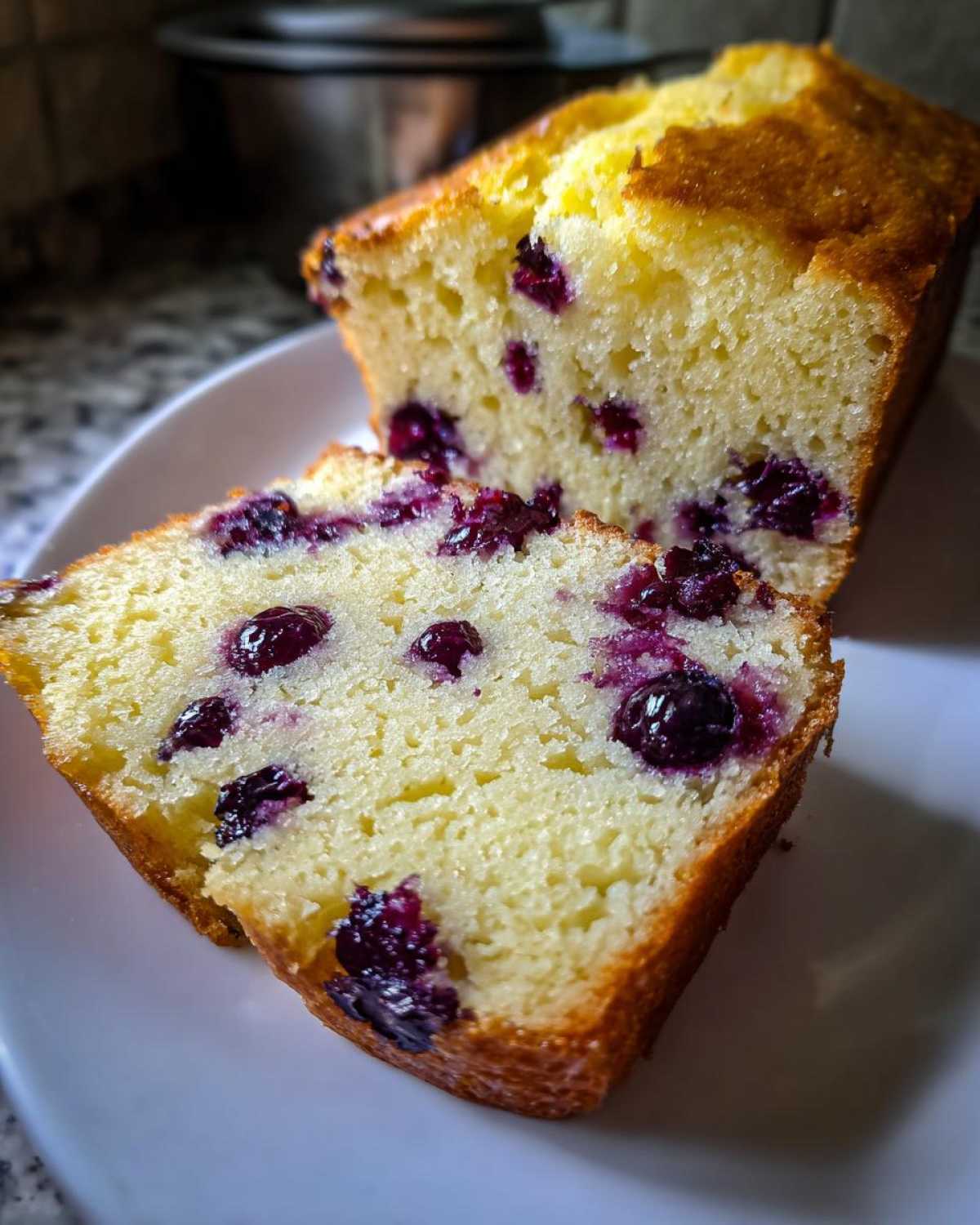Close-up of a moist slice cut from a Lemon Blueberry Yogurt Loaf, showing bright yellow crumb and juicy blueberries.