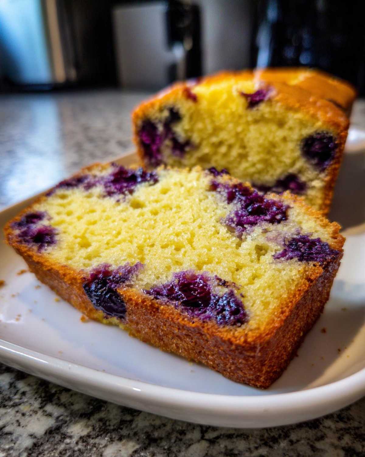 Close-up of a moist slice of Lemon Blueberry Yogurt Loaf showing bright yellow cake and deep purple blueberries.