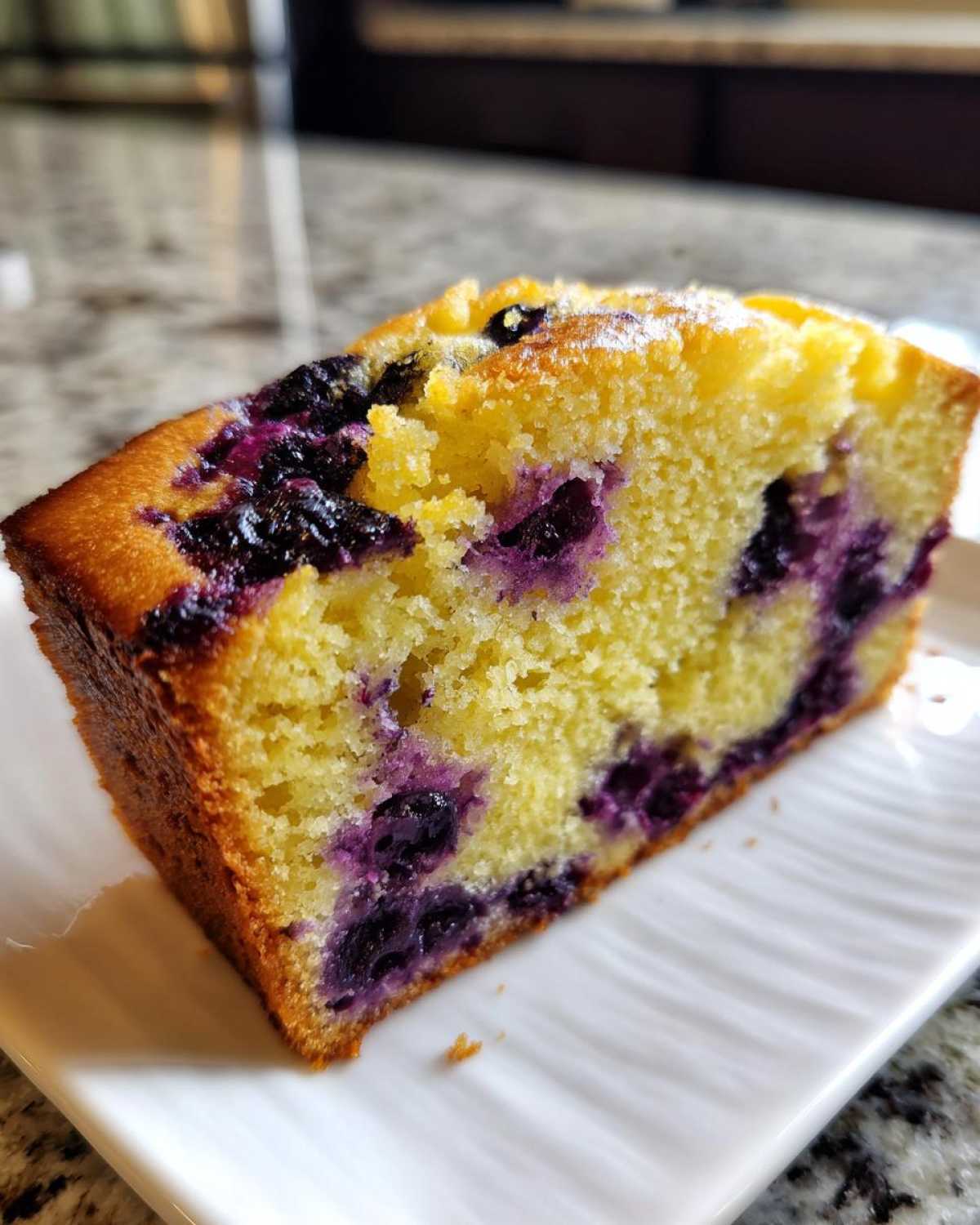 Close-up of a moist slice of Lemon Blueberry Yogurt Loaf showing bright yellow crumb and dark purple blueberries.