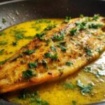 A perfectly cooked fillet of Lemon Garlic Butter Tilapia sizzling in a bright yellow lemon butter sauce.