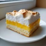 A square slice of Lemon Meringue Pie Bars showing a crust, bright yellow lemon filling, and toasted white meringue topping.