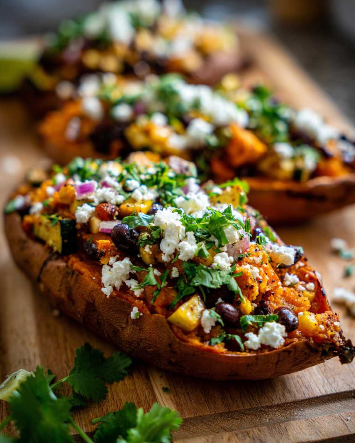 A close-up of one of the Loaded Veggie Stuffed Sweet Potatoes, topped with black beans, zucchini, feta, and cilantro.