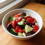 Close-up of a vibrant Mediterranean Cucumber Tomato Salad with feta cheese and Kalamata olives in a white bowl.