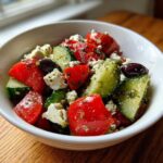Close-up of a vibrant Mediterranean Cucumber Tomato Salad with feta cheese and olives, glistening with dressing.
