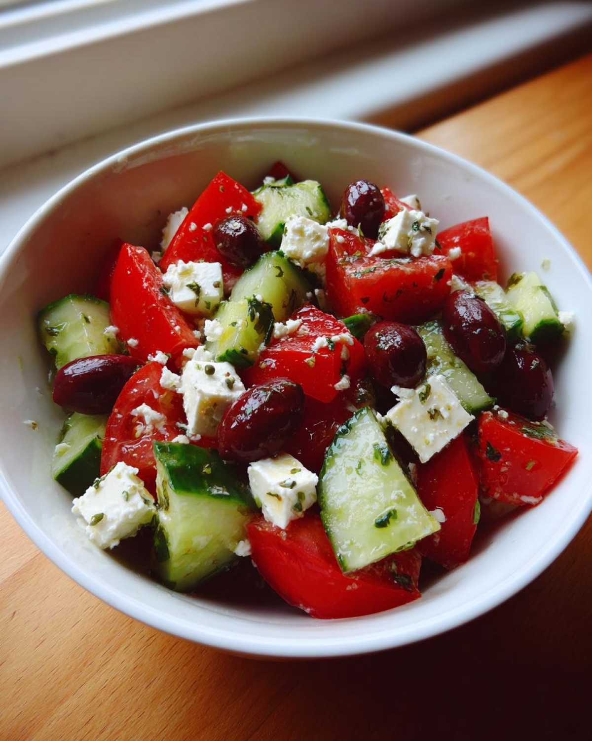 Close-up of a vibrant Mediterranean Cucumber Tomato Salad with feta cheese and Kalamata olives in a white bowl.