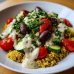 Close-up of a vibrant Mediterranean Quinoa Bowl topped with tomatoes, cucumbers, olives, and rich lemon tahini sauce.