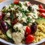 Close-up of a Mediterranean Quinoa Bowl topped with creamy lemon tahini sauce, tomatoes, cucumbers, and Kalamata olives.