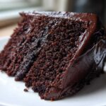 Close-up of a rich, dark slice of Gluten-Free Chocolate Cake covered in glossy chocolate frosting.