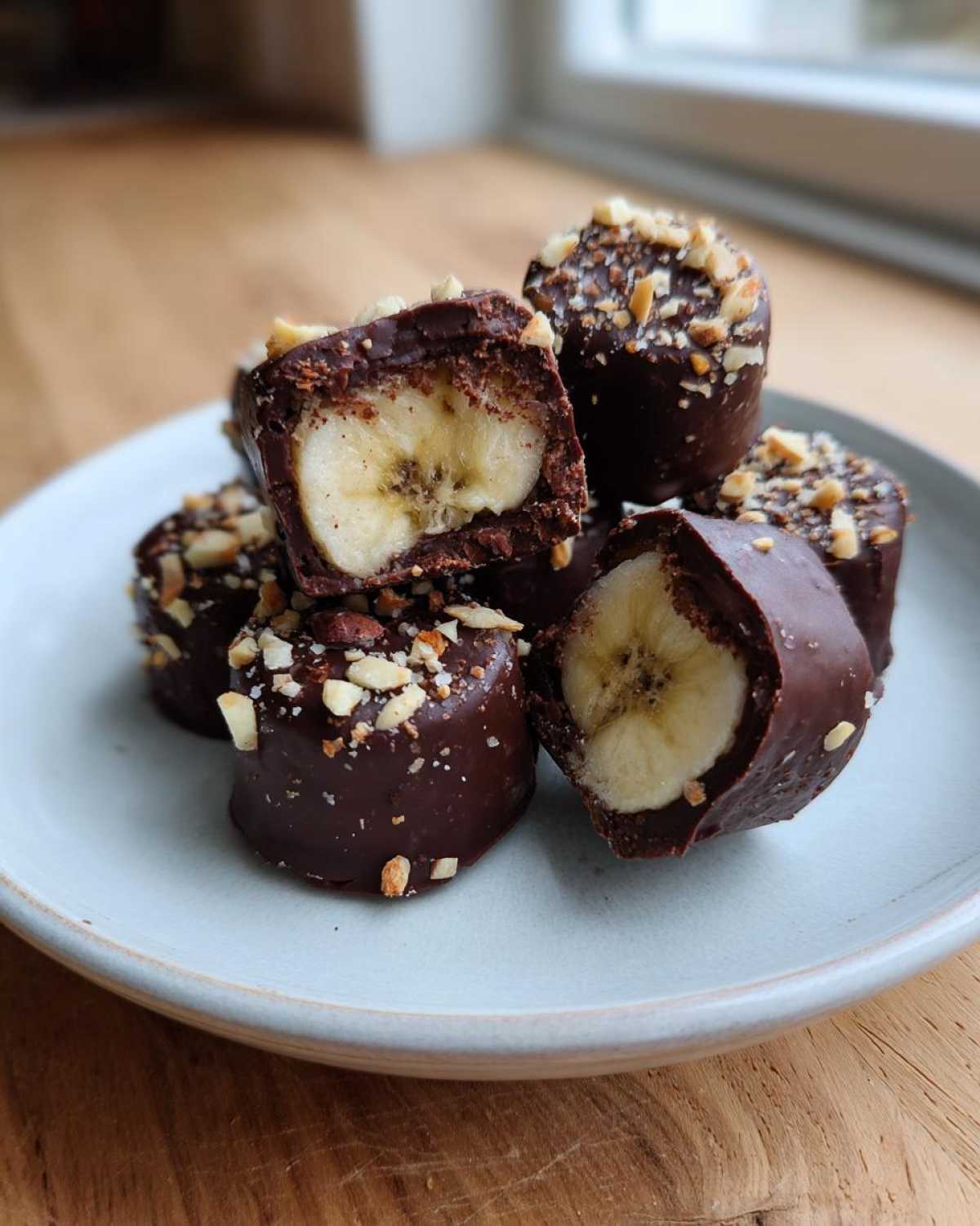 A stack of No-Bake Chocolate Covered Banana Bites dipped in dark chocolate and topped with chopped nuts.