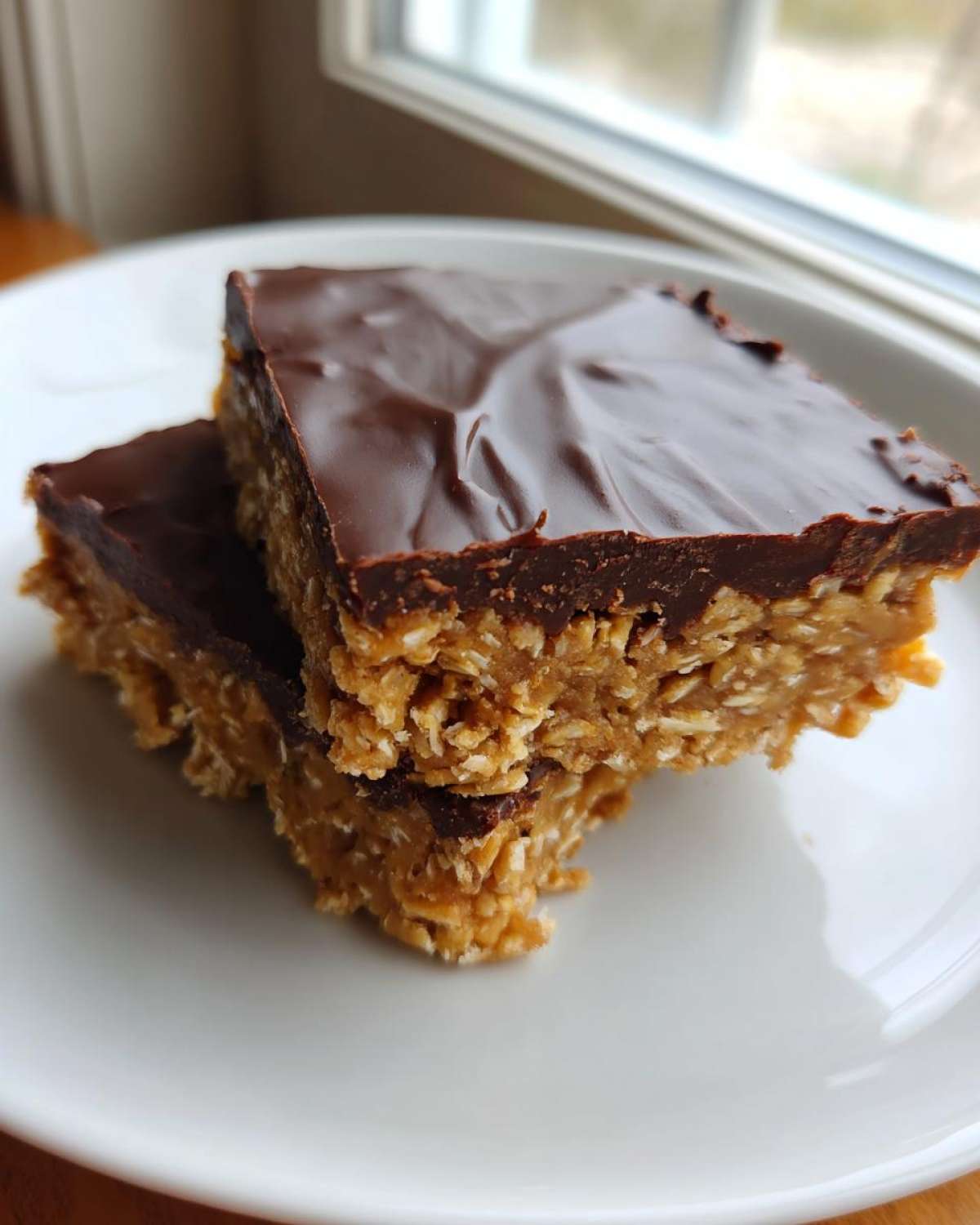 Two stacked No-Bake Chocolate Peanut Butter Oat Bars with a thick chocolate topping resting on a white plate.