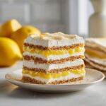 A tall slice of No-Bake Lemon Icebox Cake layered with graham crackers, lemon filling, and whipped cream.