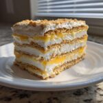 A layered slice of No-Bake Lemon Icebox Cake featuring graham crackers, lemon filling, and whipped topping.