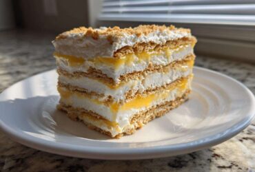 A layered slice of No-Bake Lemon Icebox Cake featuring graham crackers, lemon filling, and whipped topping.