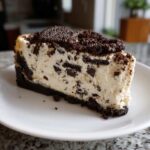 A perfect slice of creamy No-Bake Oreo Cheesecake with chunks of chocolate cookie throughout and topped with crumbs and a whole cookie.