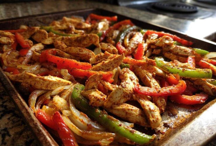 Close-up of seasoned chicken strips, red bell peppers, green bell peppers, and onions cooked together on a sheet pan for One-Pan Chicken Fajitas with Peppers and Onions.