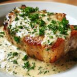 Close-up of a perfectly seared pork chop covered in creamy garlic sauce and fresh parsley.