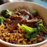 A close-up of One-Pot Beef and Broccoli Ramen Noodles in a white bowl with savory sauce.