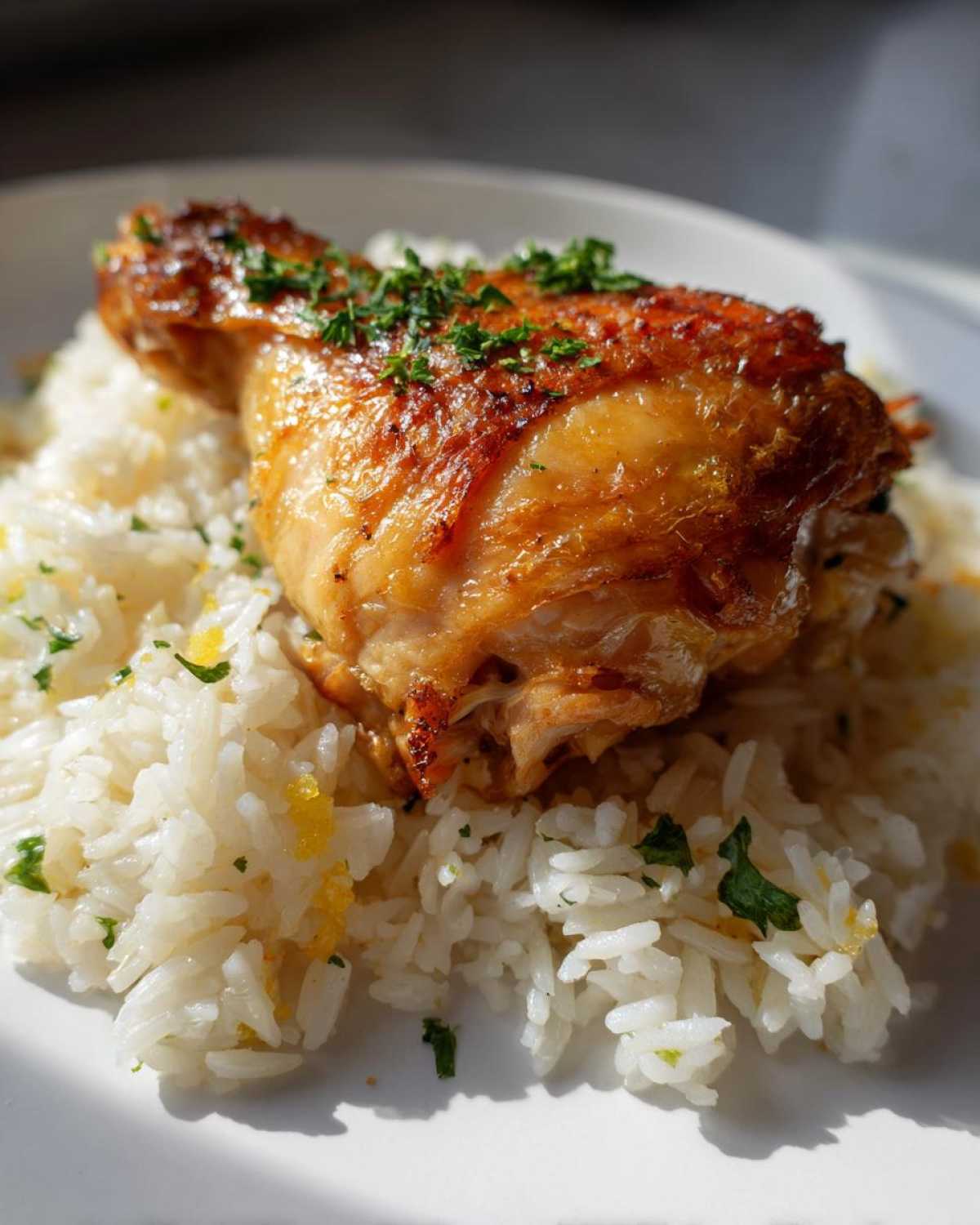 A perfectly cooked chicken leg quarter resting on fluffy white rice, garnished with parsley, from the One-Pot Chicken and Rice with Lemon and Herbs recipe.