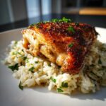 Close-up of crispy skin chicken thigh served over fluffy rice seasoned with lemon and herbs.