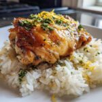 A perfectly cooked piece of chicken served over white rice, garnished with lemon zest and fresh herbs for One-Pot Chicken and Rice with Lemon and Herbs.