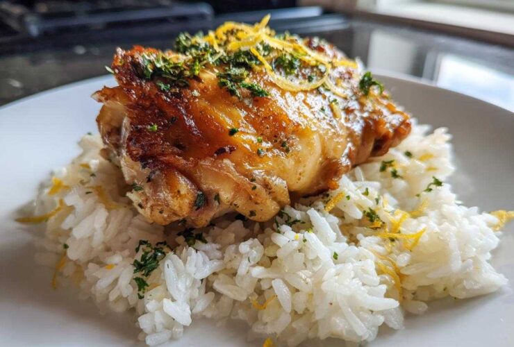 A perfectly cooked piece of chicken served over white rice, garnished with lemon zest and fresh herbs for One-Pot Chicken and Rice with Lemon and Herbs.