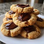 A close-up stack of freshly baked Peanut Butter Blossom Cookies topped with melted chocolate centers.
