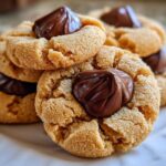 A stack of freshly baked Peanut Butter Blossom Cookies topped with melted chocolate kisses on a white plate.