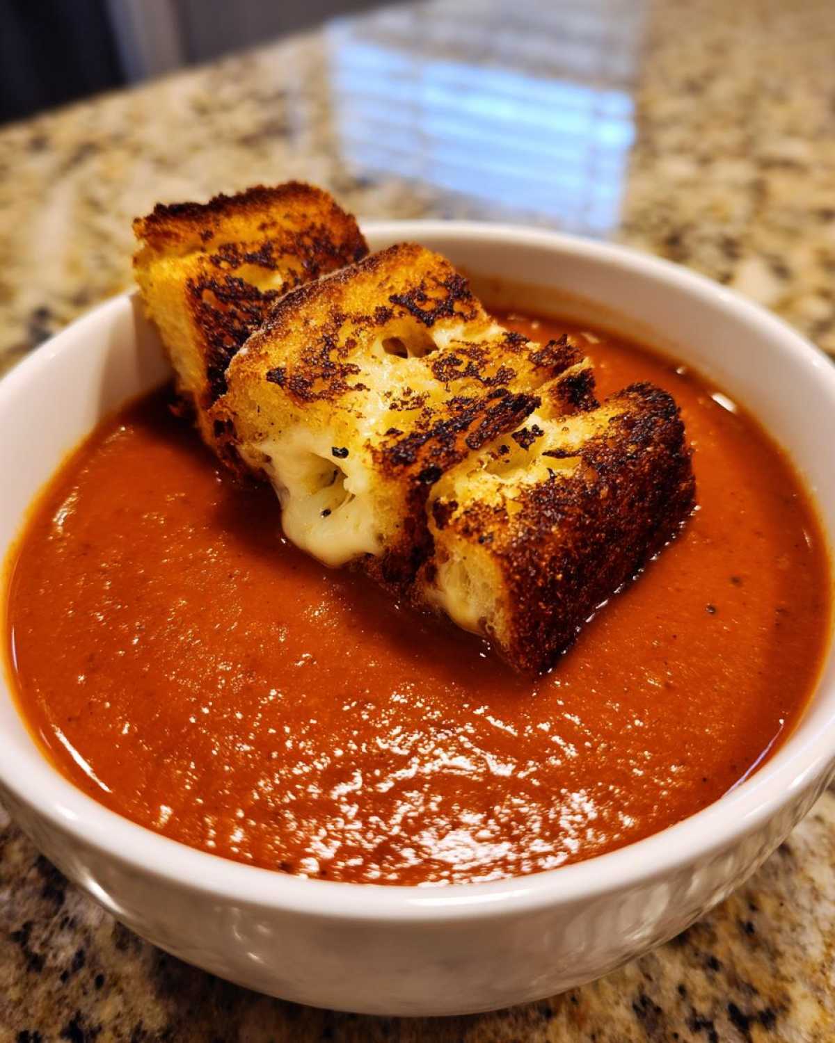 Close-up of a bowl of rich, red Roasted Tomato Basil Soup topped with crispy Grilled Cheese Croutons.