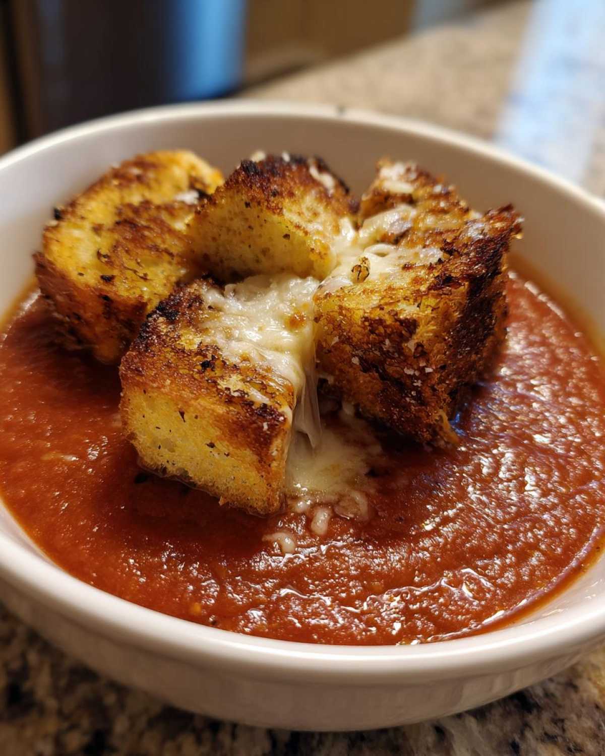 Close-up of Roasted Tomato Basil Soup topped with cheesy, golden brown grilled cheese croutons.