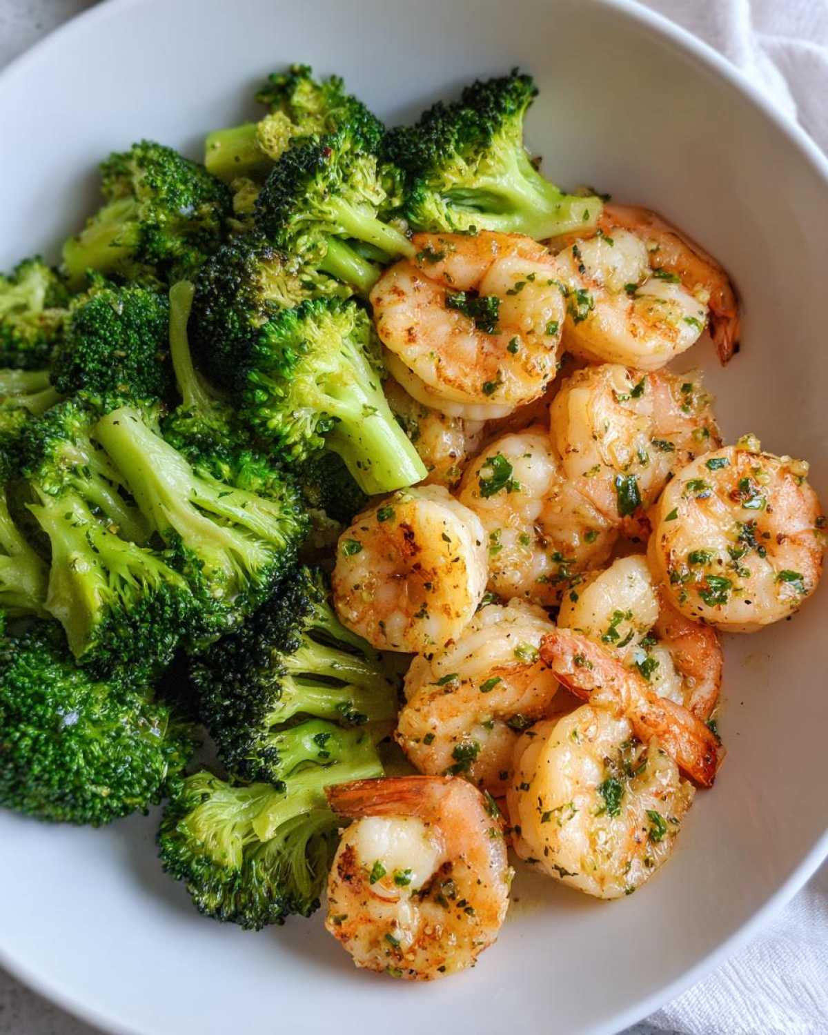 Close-up of cooked shrimp and bright green broccoli florets seasoned with garlic and parsley, ready to eat.