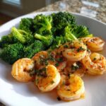 Close-up of cooked shrimp coated in garlic butter and parsley next to bright green broccoli florets.