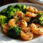 Close-up of cooked shrimp and bright green broccoli florets coated in garlic butter sauce.