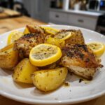 Close-up of crispy Sheet Pan Lemon Pepper Chicken and Potatoes garnished with lemon slices.