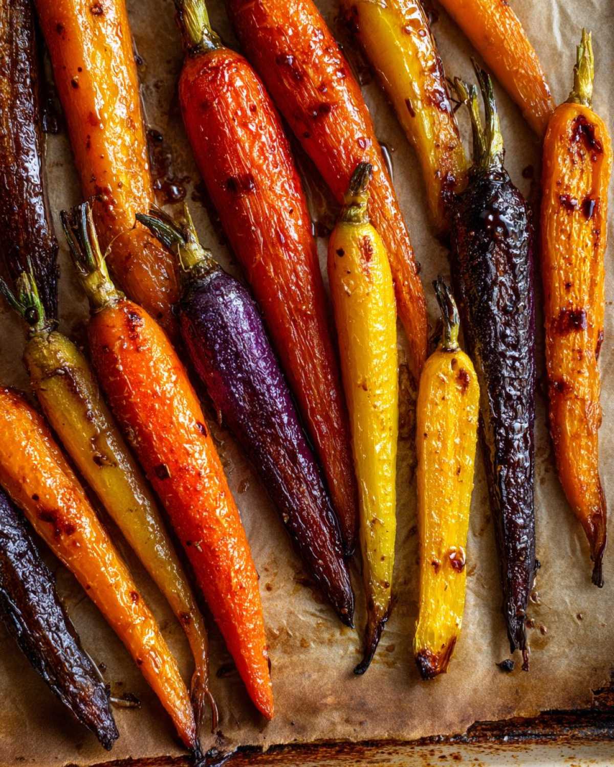 Close-up of glossy, glazed Sheet Pan Roasted Rainbow Carrots with Honey on parchment paper.