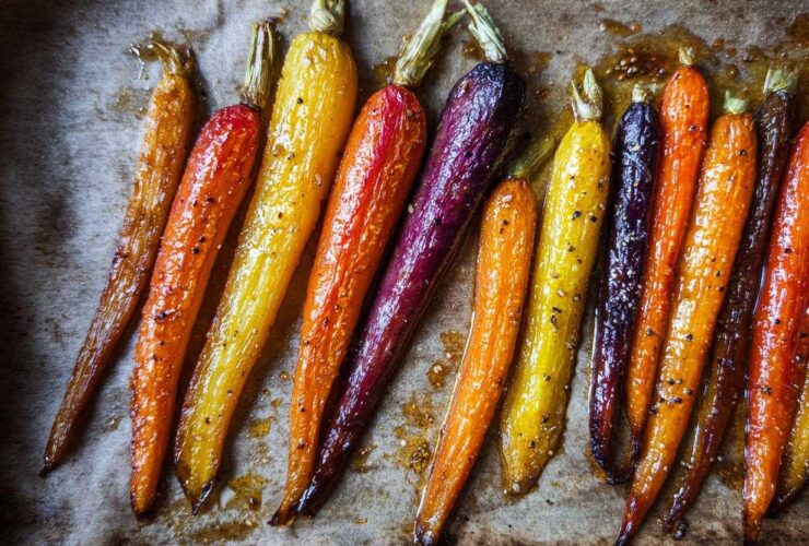 Close-up of glossy Sheet Pan Roasted Rainbow Carrots with Honey, showing orange, yellow, and purple varieties on parchment paper.