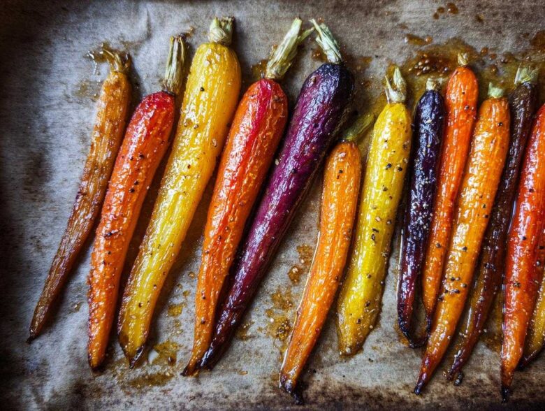 Close-up of glossy Sheet Pan Roasted Rainbow Carrots with Honey, showing orange, yellow, and purple varieties on parchment paper.